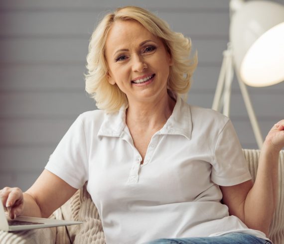 Beautiful old woman Beautiful old woman in casual clothes is holding a credit card, using a laptop and smiling while sitting at home