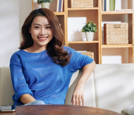 Portrait of beautiful young Asian woman sitting on sofa at home
